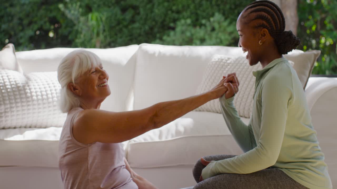 Avó e neta afro-americana sorrindo, batendo as mãos, de mãos dadas e criando laços no chão ao lado do sofá