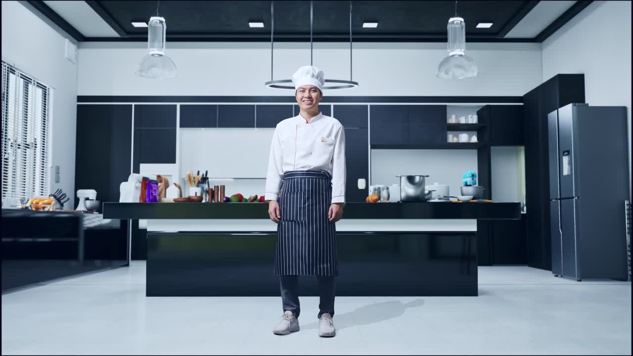 cuerpo lleno de hombre asiático chef de pie y sonriendo a la cámara en la cocina de casa