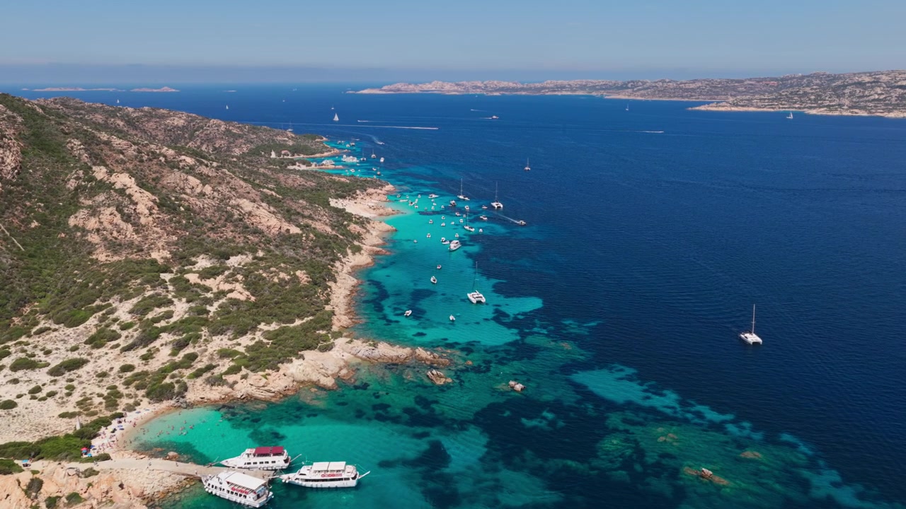 Vue aérienne spectaculaire de yachts à voile de luxe dans un détroit aux eaux bleu turquoise, longeant des falaises de granit et le littoral rocheux de l'île de Spargi dans l'archipel de la Maddalena en Sardaigne, Italie