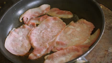 delicious slices of bacon cooking gently in hot pan with bubbling oil as camera rotates. cooked breakfast morning food.