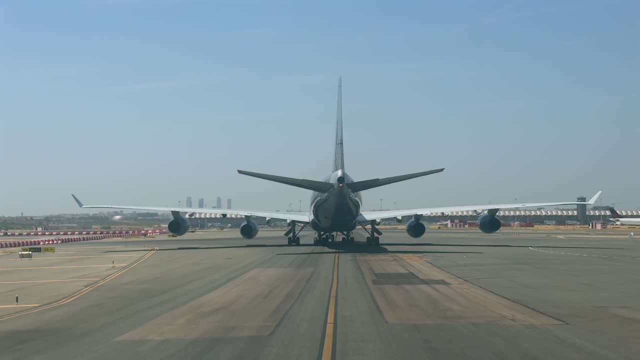 A massive 4-engine jumbo jet taxiing slowly along Madrid airport taxiway in a extremely hot and hazy summer afternoon. Shot taken from another jet cockpit taxiing behind