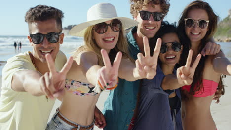 group of friends smiling and making peace sign at camera for a portrait on the beach