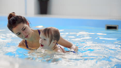 cute blonde toddler in protective glasses is diving under the water together with his mother in the swimming pool trying to take out his toy. his mother is teaching him how to swim. an underwater shot.