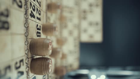 un video macro vertical de un tablero de bingo, luces de estudio, 120 fps, cámara lenta, dígitos de chips de madera, imágenes en bruto, juego de mesa de lotería vintage, números de cartas, deslizamiento de grúa derecho movimiento suave