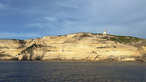 sunlight on cliff of capo pertusato lighthouse in corsica island as seen from sailing boat, france