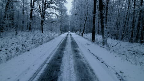 Drone-low-angle-Fast-flying-back-alone-the-frozen-and-covered-with-snow-forest-road-in-Pieszkowo,-Poland