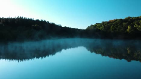 early morning low drone shot over glossy lake with some fog-4
