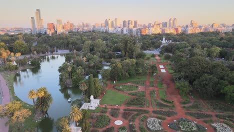 aerial dolly out of people walking in palermo woods street, rosedal gardens and pond at sunset, buenos aires