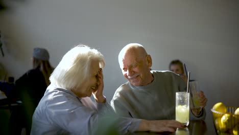 side view of a senior couple drinking limonade and talking while they are sitting in a bar at sunset