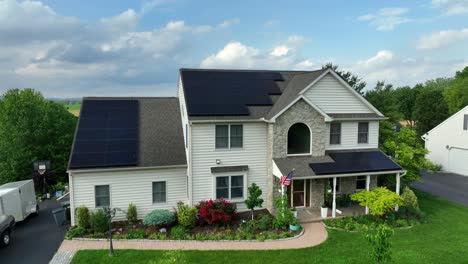 proud family living in single family hose with modern solar panels on roof. american flag on porch of building in rural area of united states. green trees and colored rural farm fields in background.