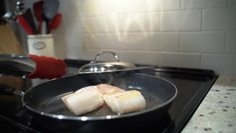 fish frying in a pan when a woman reaches in to flip with a metal tongs