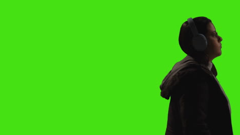 woman wearing wireless headphones streaming music from mobile phone walking across frame against green screen 1