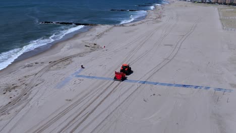 an aerial view of an orange tractor raking an empty beach on a sunny day