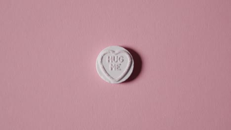 mano recogiendo caramelos de corazón con un mensaje de abrazo sobre fondo rosa