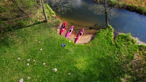 Red-kayaks-parked-on-the-bank-of-a-wild-river,-aerial-view