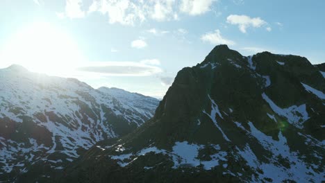 majestic snow-covered mountains, bright sun creates lens flare over rugged peaks, italian alps, italy. aerial drone panoramic view