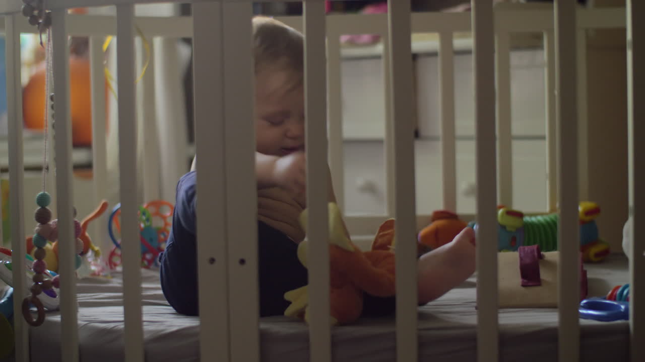 A baby girl in blue pants playing with a toy in a crib
