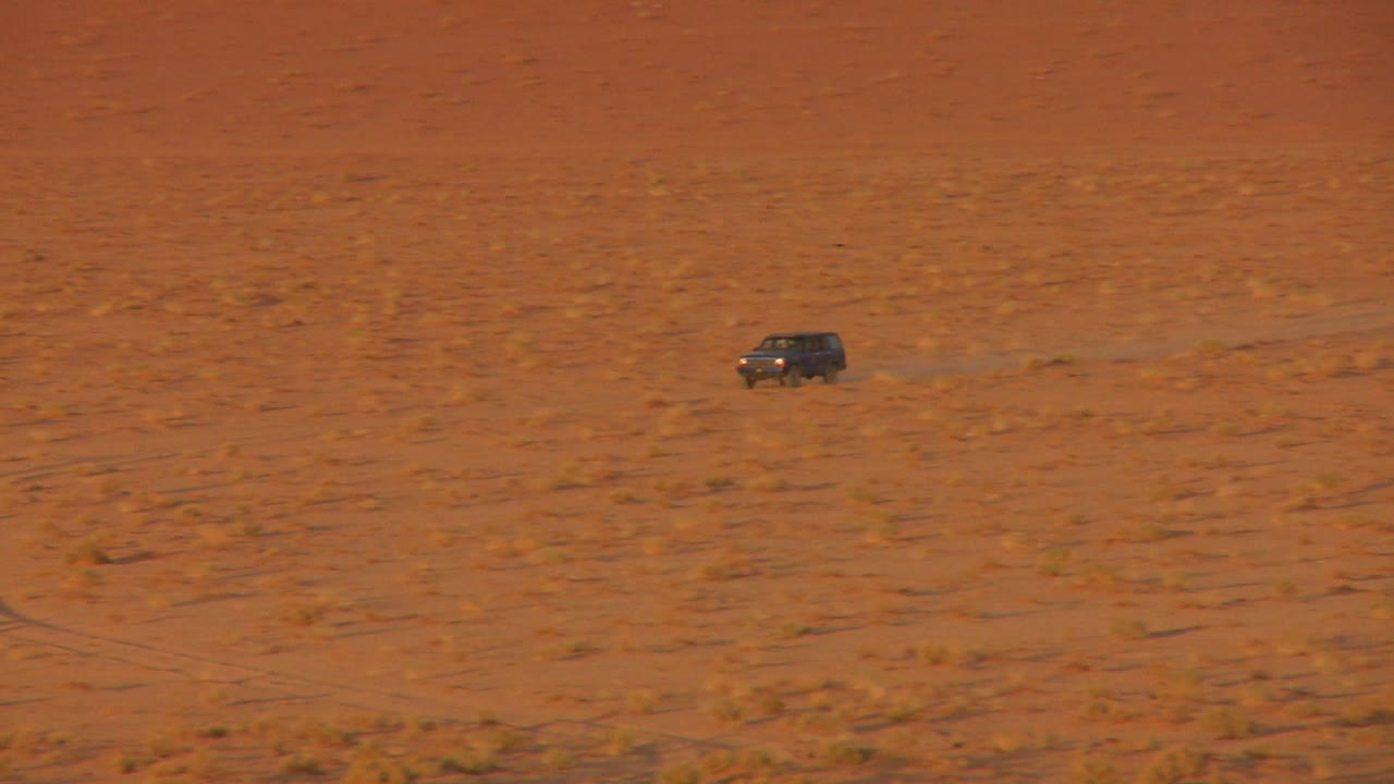 확대하여 요르단 와디 럼의 광활한 사막 모래 위를 빠르게 달리는 베두인 트럭을 보여줍니다.