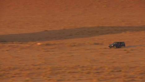 Zoom-Hacia-Atrás-Para-Revelar-Un-Camión-Beduino-Conduciendo-Rápido-A-Través-De-Las-Vastas-Arenas-Del-Desierto-De-Wadi-Rum-Jordan