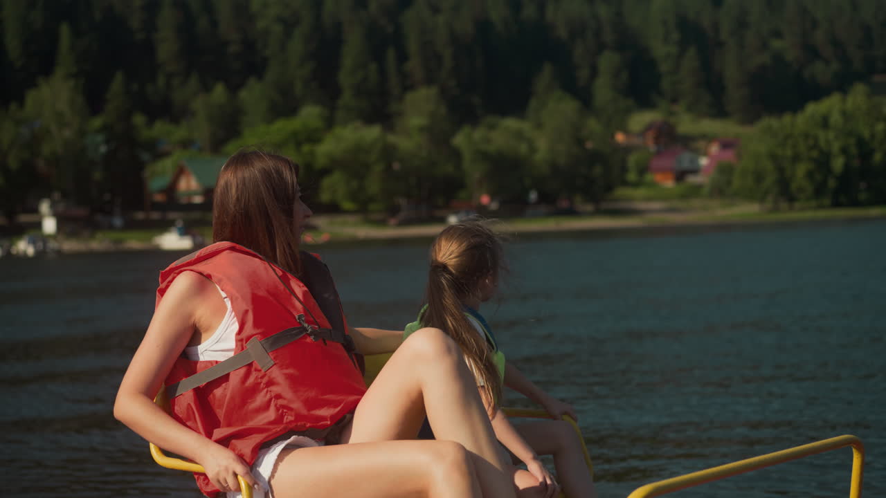 madre e hija miran a la orilla con árboles altos moviéndose en catamarán. joven y niña con chalecos protectores charlan admirando el paisaje desde el transporte acuático en cámara lenta