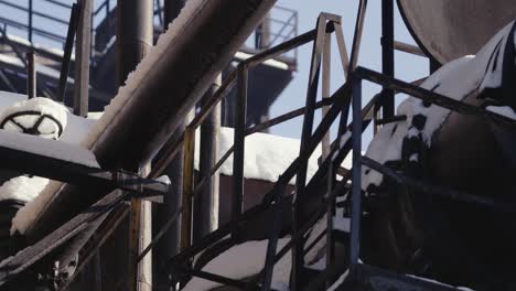 Industrial-setting-with-various-dark-coloration-metal-structures-and-pipes-covered-with-melting-snow