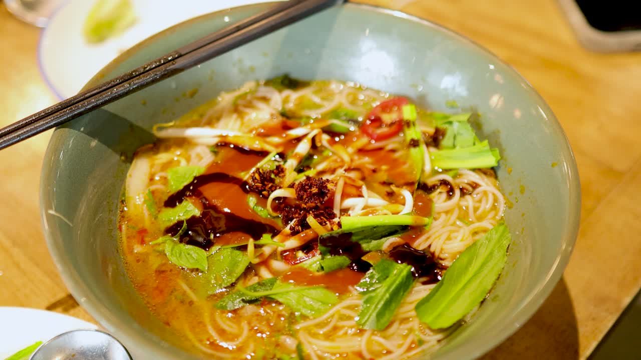 A bowl of vibrant Vietnamese pho with meat and fresh herbs in a Bangkok restaurant, captured in warm lighting