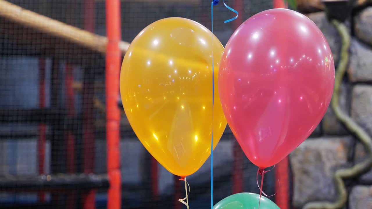 globos de fiesta de cumpleaños amarillos y rosas con azul y verde fuera del marco flotando con un lugar de juego para niños en el fondo - en el cine 4k