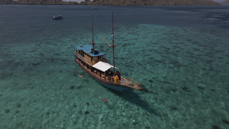 Vista-Aérea-De-Un-Turista-Nadando-Alrededor-Del-Bote-De-Madera-En-El-Océano-Indonesio