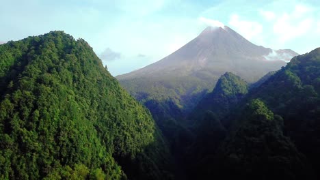 Vuelo-Aéreo-Lento-Hacia-Adelante-Hacia-La-Colina-Cubierta-Y-El-Volcán-Merapi-En-El-Fondo-Durante-El-Día-Soleado