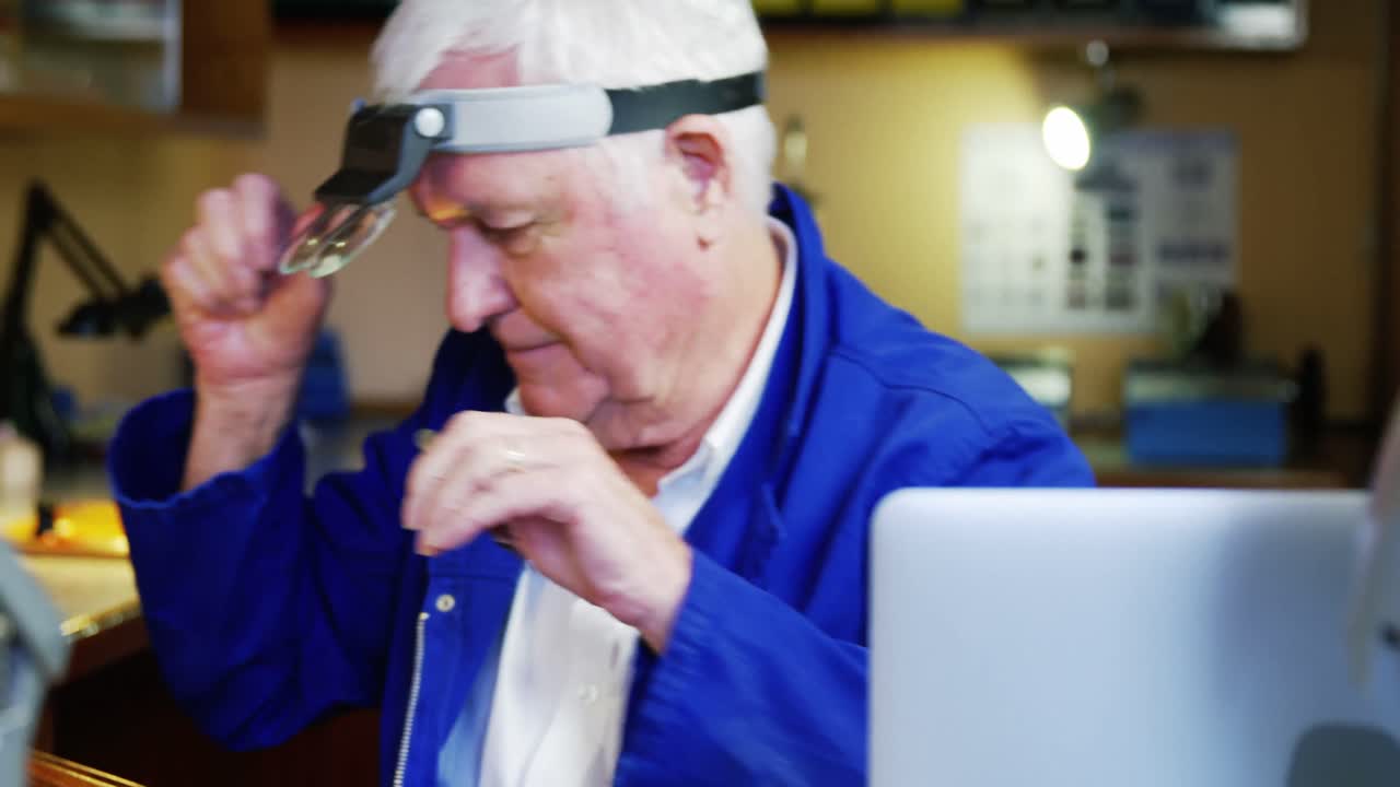 Horologist using laptop while repairing a watch