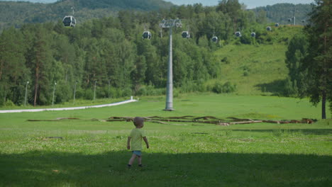 little boy walks along meadow under contemporary ropeway