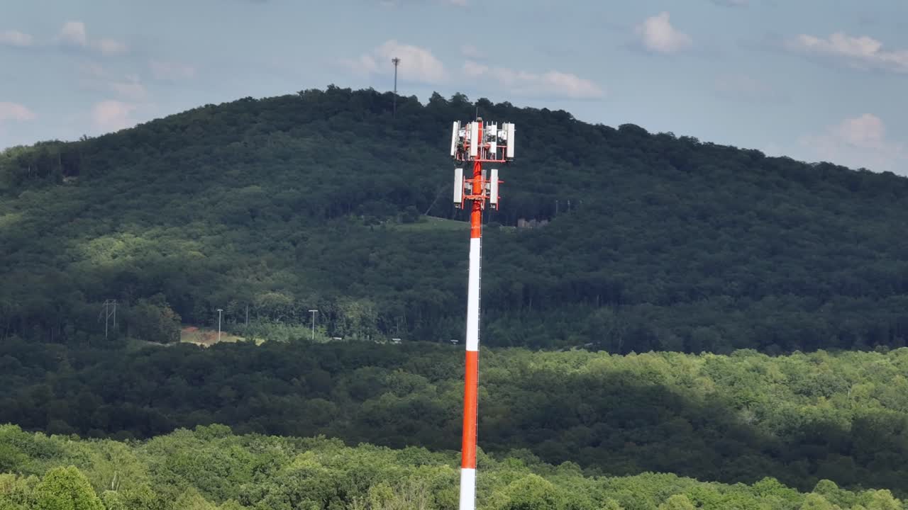 Aerial view of red white cell tower in nature of USA. Sunny summer day in suburb. Transmit signals for mobile phones and devices in area