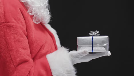 Video-of-santa-claus-holding-christmas-present-with-copy-space-on-black-background