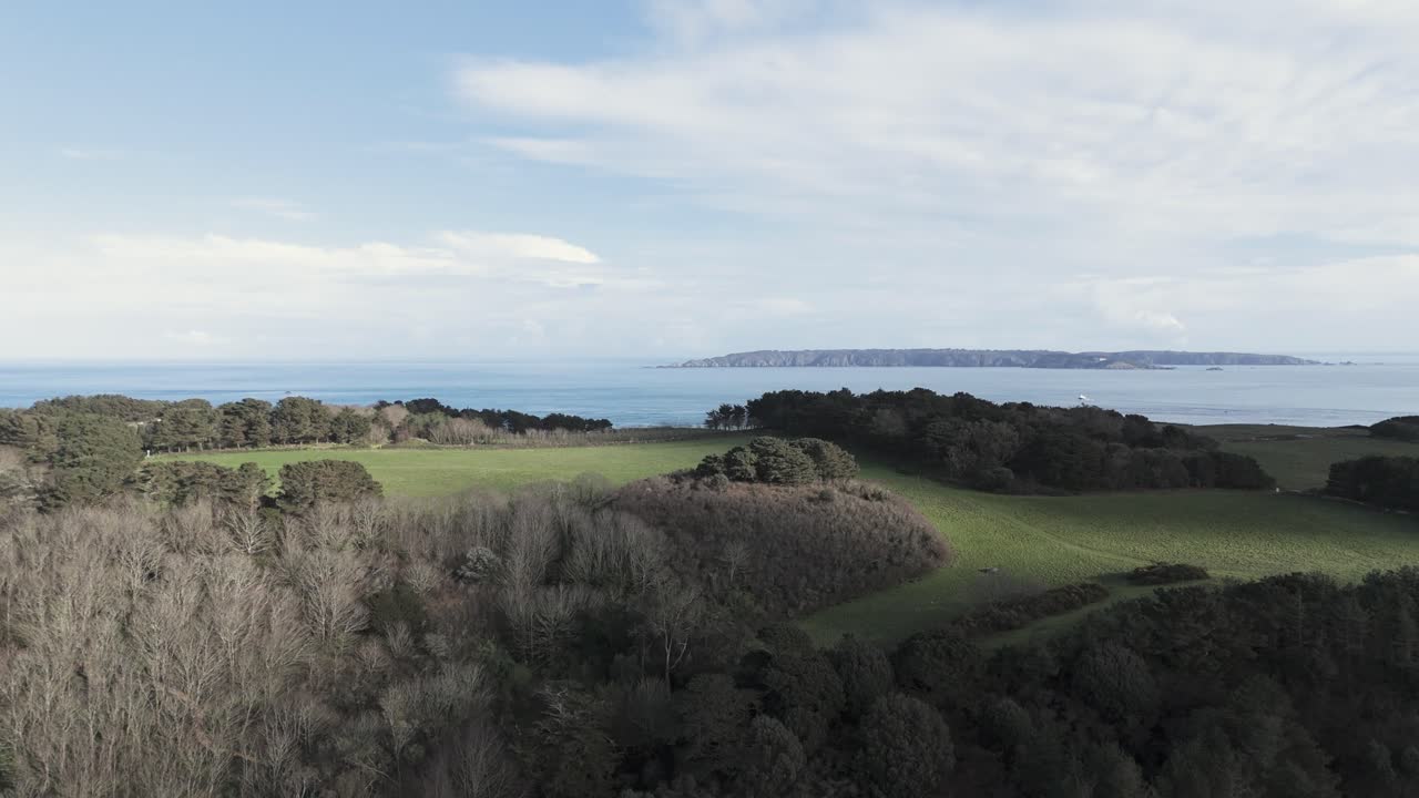 Flight over Herm Island, Channel Islands view towards Sark and panning over the Island with trees and fields to Shell Beach at low tide with clear calm sea