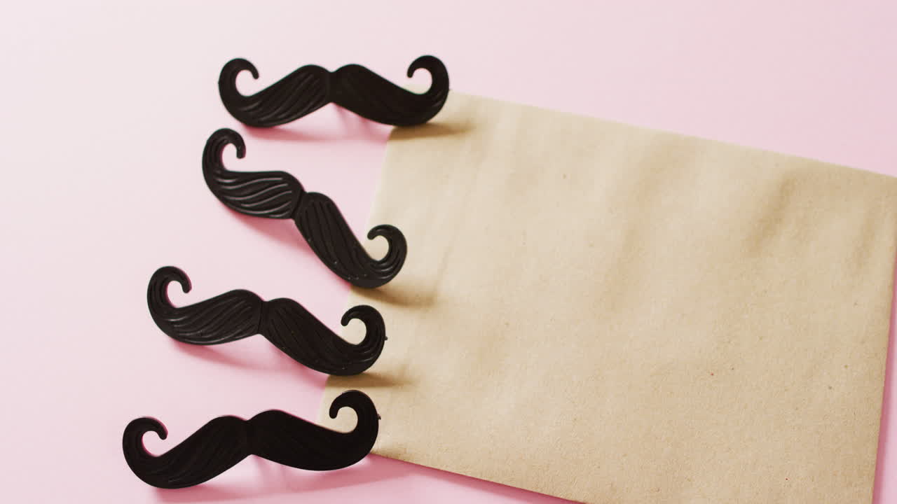 4개의 검은색 가짜  ⁇ 수염과 분홍색 배경에 복사 공간이 있는 노란색 봉투의 비디오