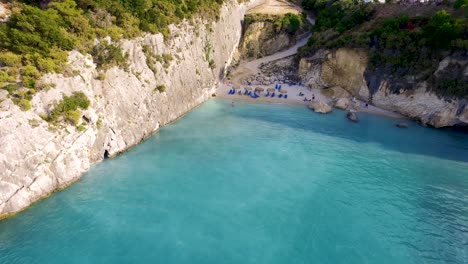 Playa-Xigia-En-Zakynthos,-Aguas-Turquesas-Rodeadas-De-Acantilados-Y-Bañistas-Disfrutando-Del-Sol,-Vista-Aérea