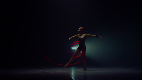 mujer flexible girando la mano con la cinta. mujer deportista bailando en el espacio oscuro.