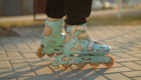 un primer plano capturando los pies de una persona usando patines, deslizándose suavemente a lo largo de un camino pavimentado en un parque durante la puesta de sol