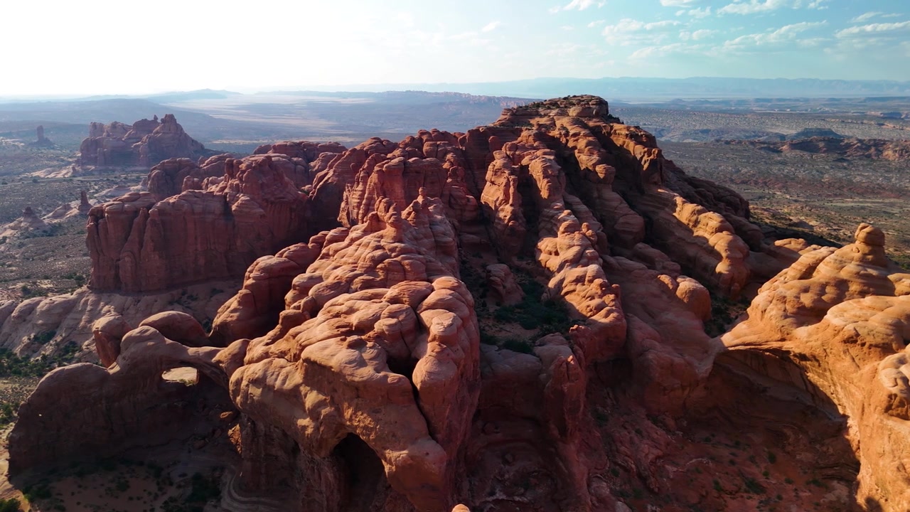 Splendido filmato stock del Parco Nazionale di Arches, USA, durante un pomeriggio luminoso. La luce solare brillante illumina le maestose strutture di arenaria rossa e il paesaggio desertico sotto un cielo azzurro limpido.
