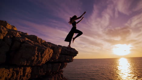 woman jumping off cliff at sunset