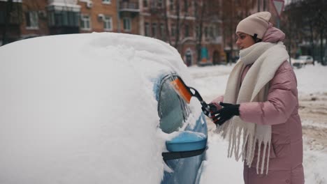 woman removing snow from a car in winter