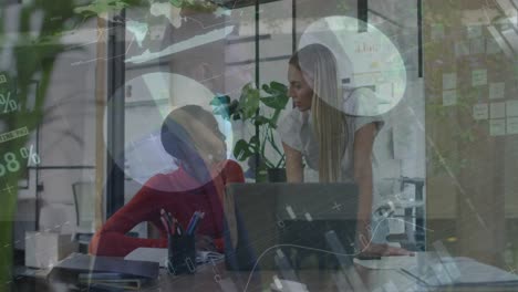 Statistical-data-processing-against-two-diverse-female-office-colleagues-discussing-at-office