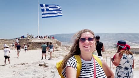 woman with windswept hair and greek flag at acropolis, athens, greece