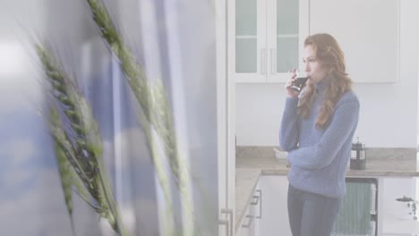 Animation-of-grain-over-caucasian-woman-drinking-coffee-in-kitchen