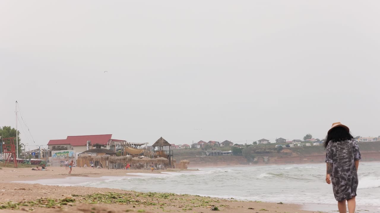 루마니아 바마 베체에서 극심한 파도와 함께 흑해 연안의 해변을 걷고 있는 여성 관광객