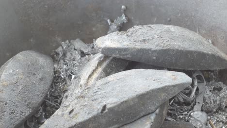 hands melting lead over a metal container, with fumes rising, in a craftsmanship process, close up