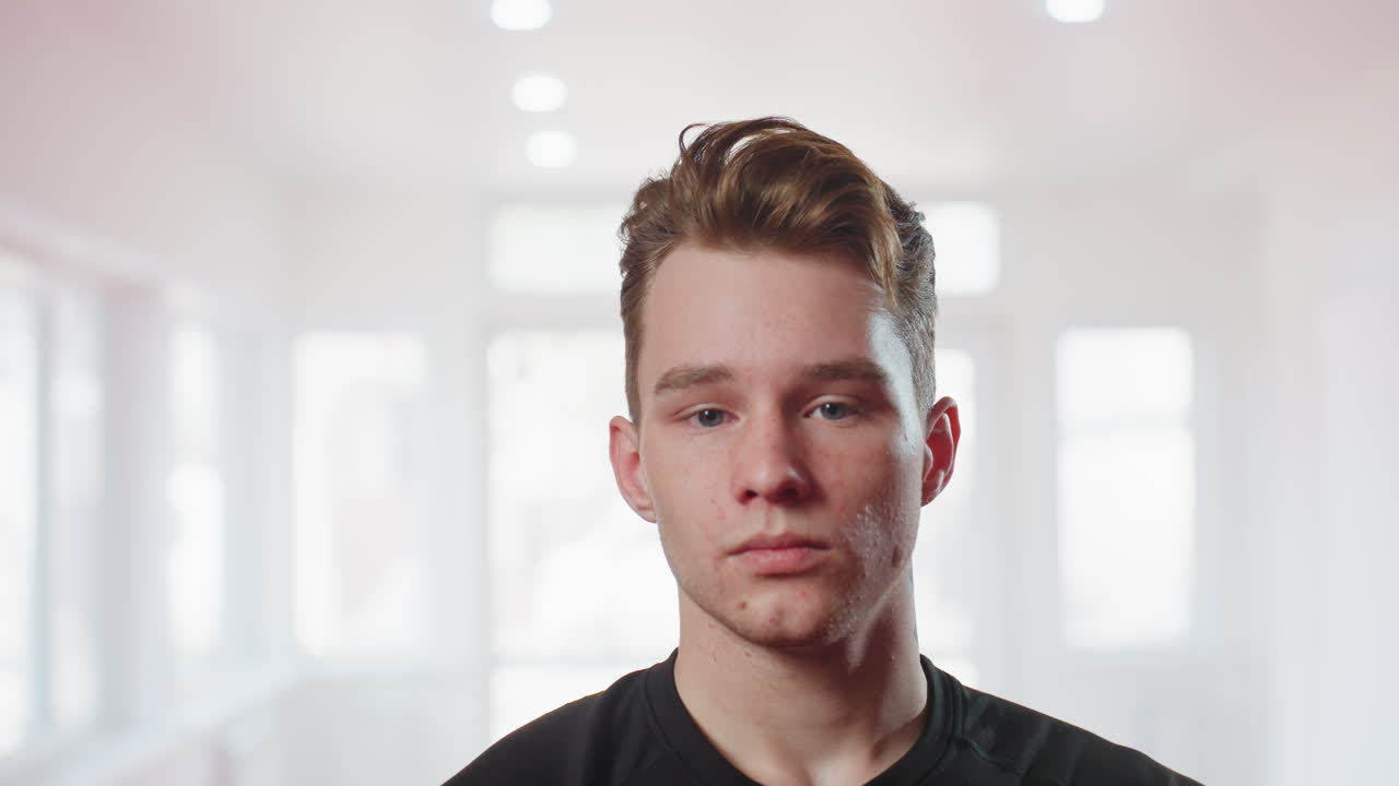Soldier in black athletic shirt standing in bright gym with focused expression, hands clasped, looking to side, symbolizing readiness, discipline, mental strength, preparation before training session