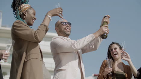 happy employees opening champagne with splashes during party