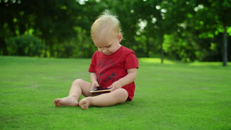 手に携帯電話を持った可愛い幼児 ⁇ 緑の草の上に座っている陽気な少年 ⁇