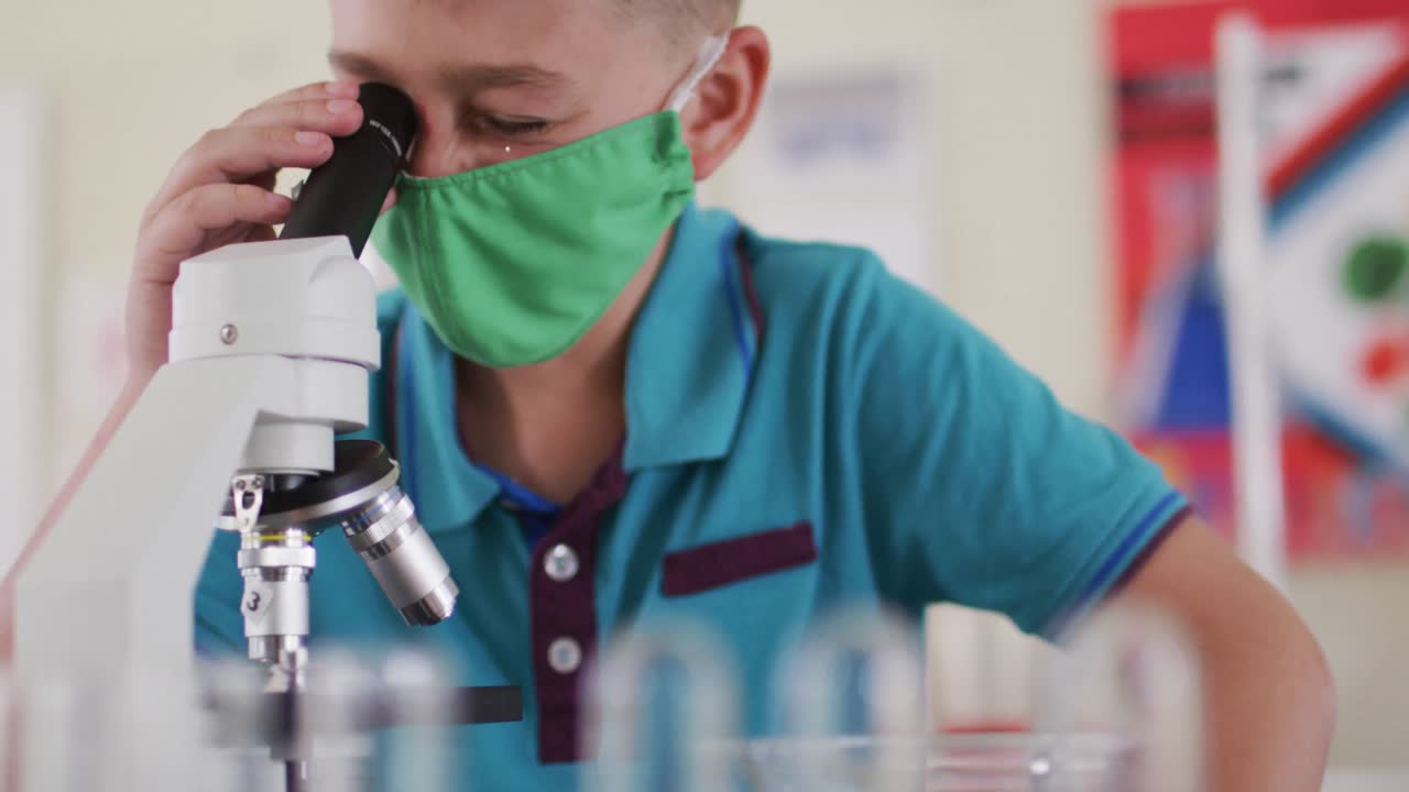 niño con máscara facial y gafas de protección usando microscopio en el laboratorio